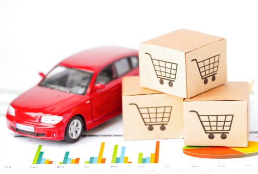 Toy red car on a piece of paper with graphs on it, next to a set paper boxes with shopping trolleys on them