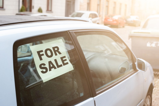 A white car on a street with a 'For sale' sign in the window of the car